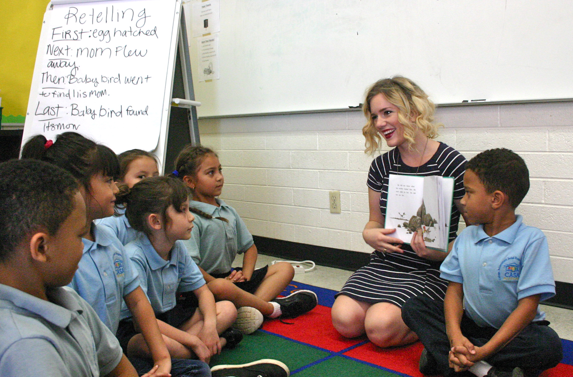 Profesor sentado en una alfombra con alumnos mostrando un libro
