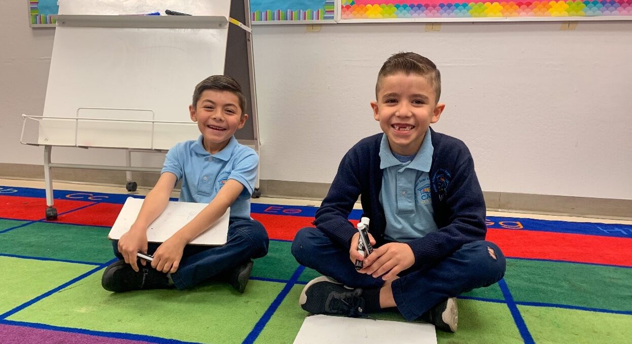 2 scholars at CASA Academy smile on their classroom carpet